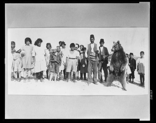 Group portrait of dancing bear, trainer, and children at Floria Beach, Istanbul, Turkey, 1915 [Frank and Frances Carpenter Collection (Library of Congress)]